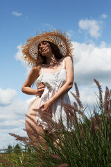 Young sexy beautiful woman in a straw hat standing and enjoying the bright sun in the garden...