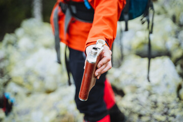 Person hikes rocky trail with flask in hand, enjoying outdoor adventure