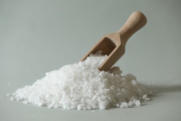 Organic salt and wooden scoop on light grey background, closeup