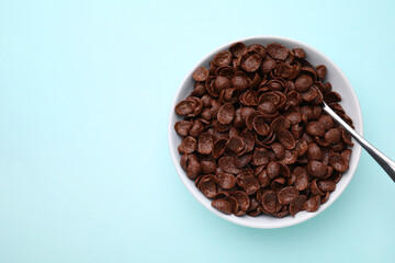 Breakfast cereal. Chocolate corn flakes in bowl and spoon on light blue table, top view. Space for text