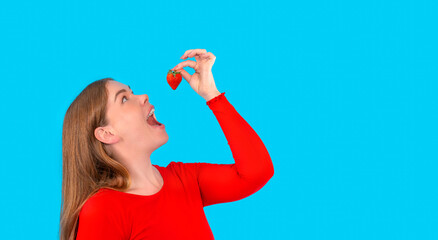 happy curvy woman eating strawberries with open mouth and face up on blue background with copy...