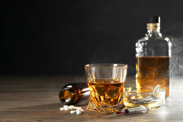 Alcohol and drug addiction. Whiskey in glass, syringe, pills and cigarettes on wooden table, space for text