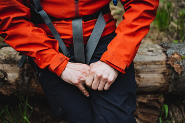 A person in black pants and an orange jacket sits on a log in nature
