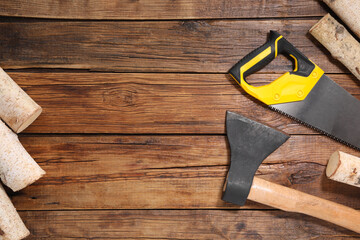 Saw with yellow handle, axe and firewood on wooden background, flat lay. Space for text
