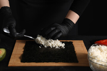 Chef in gloves making sushi roll at dark table, closeup