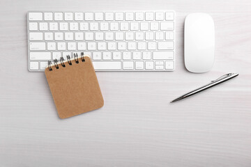 Office workplace. Keyboard, pen, mouse and notebook on white wooden table, flat lay. Space for text