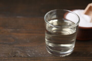 Vinegar in glass and baking soda on wooden table, closeup. Space for text