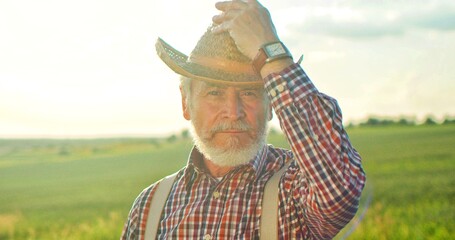 Portrait of the caucasian professional senior farmer wearing hat standing in backyard of organic...