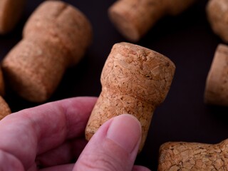 A person fingers holding a champagne cork against a black background with other corks nearby