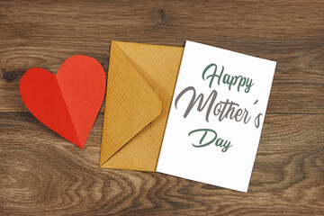 Mother's Day decorations concept. Top view photo of white invitation card with red heart shape paper on wood table