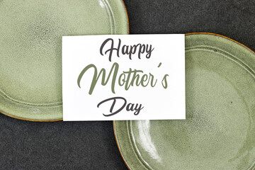 Mother's Day decorations concept. Top view photo of white invitation card with green ceramic plate