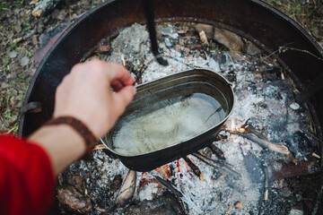 Using an automotive tire as a pot, the person is cooking food over a fire