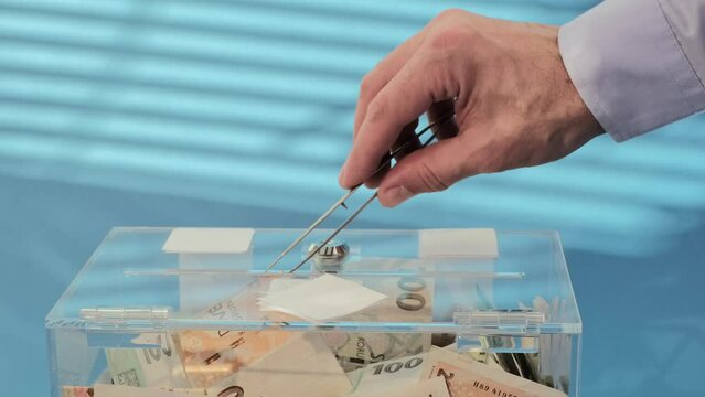 Theft of money from donations. A hand retrieves money with tweezers from a donation box 200 Czech krona banknote