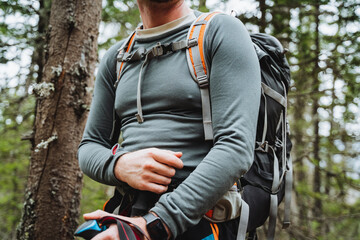 A man wearing sportswear and sunglasses stands in the woods with a backpack