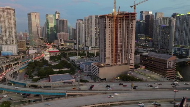 Establishing aerial shot of vehicles driving on Downtown I95 Riverside multilane highway at sunset with Miami skyline view. Drone flight over multi-level intersection Miami Florida