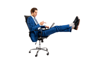 A smiling man in a blue suit seated on an office chair with legs up, using a laptop, isolated on a white background, concept of relaxed business