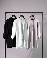 Three t shirts on hangers hanging from clothes rail and copy space on grey background. Fashion, clothes, colour and fabric concept.