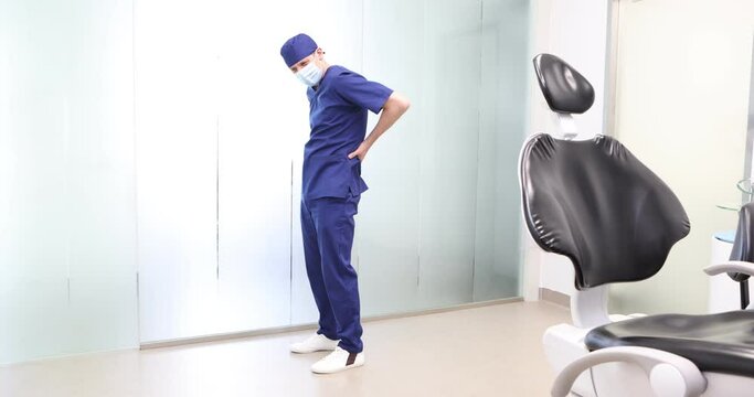Standing dentist, dealing with lower back pain.Symptoms and self help exercises, stretching. Profile view.