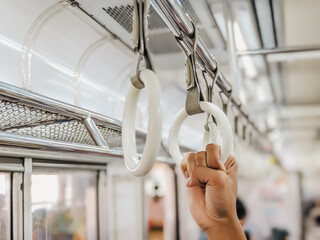 Selective focus of a hand of a young asian man holding onto grab handle inside the train. Public...