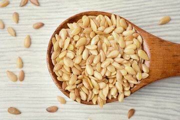 Close up photograph of the golden linseeds or flaxseeds in wooden spoon on white textured wooden background.