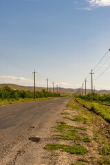 Fototapeta na wymiar A road with a few trees in the background and a few wires above it. The road is empty and the sky is clear
