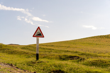A sign with a red triangle and the number 12 on it is standing in a field. The sign is warning of a steep drop off