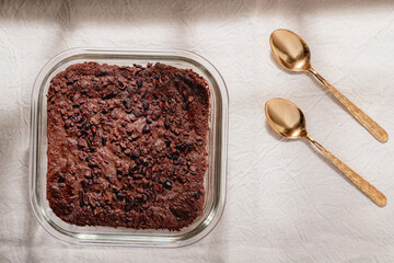 baked brownie on glass baking dish with cacao nibs topping and two golden spoons