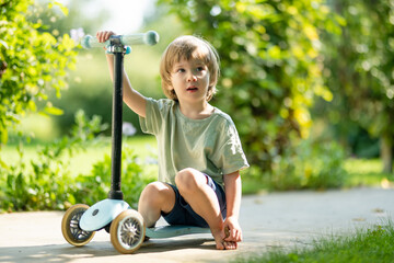 Adorable little boy riding his scooter in a back yard on summer evening. Young child riding a...