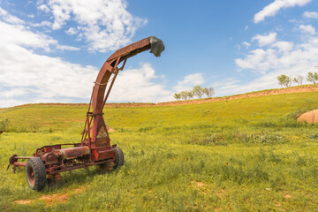A red tractor is sitting in a field of grass. The tractor is old and rusted, and it is surrounded...