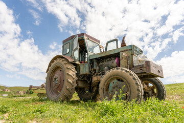 An old tractor is parked in a field. The tractor is rusty and has a large wheel. The sky is blue and there are clouds in the background