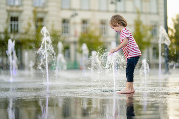 Cute little boy having fun with water in city fountain. Child playing water games outdoors on hot...