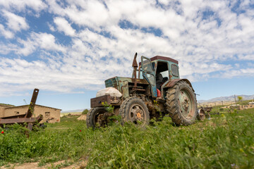 An old tractor is sitting in a field with a cloudy sky in the background. The tractor is rusted and he is abandoned