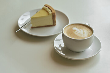 A cup of hot cappuccino latte with a piece of cake on the table.