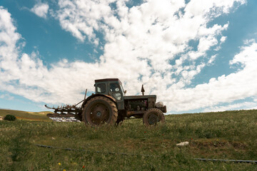 A tractor is in a field with a cloudy sky in the background. The tractor is old and has a lot of dirt on it
