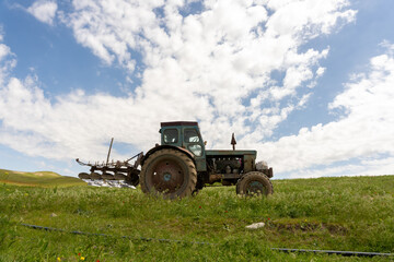 Fototapeta premium An old tractor is parked in a field. The sky is clear and blue, and the sun is shining brightly