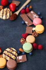 Macarons, chocolate, cookies, berries and various nuts on dark blue background. Selective focus.