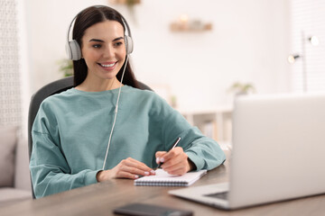 Young woman in headphones watching webinar at table in room