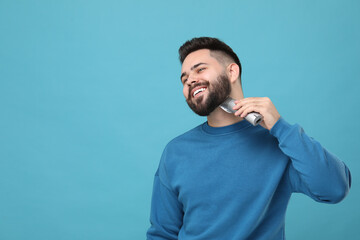 Handsome young man trimming beard on light blue background. Space for text