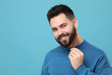 Handsome young man combing beard on light blue background. Space for text