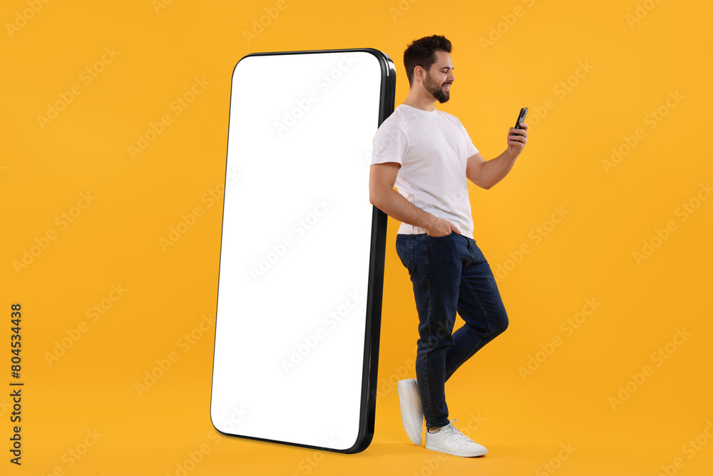 Aufkleber man with mobile phone standing near huge device with empty screen on dark beige background. mockup f