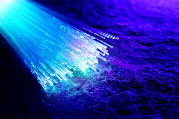 Optical fiber strands transmitting different color light on textured background, closeup. Space for...