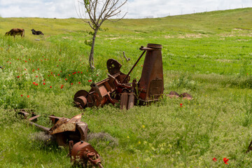 A rusty old tractor is sitting in a field of grass. The tractor is surrounded by other old farm...