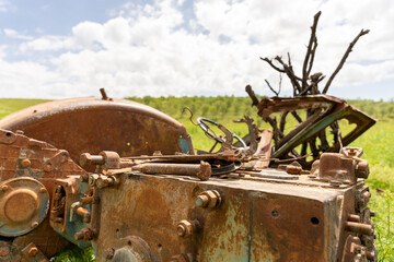 A rusted old tractor sits in a field with a pile of branches next to it. Concept of abandonment and decay, as the tractor and branches have been left to rust and decay in the open field