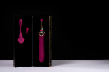 Box with a stylish burgundy masturbation dildo on a white table against a black background. A set...