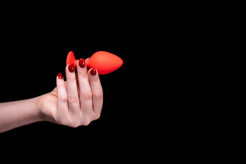 Red anal plug in a female hand on a black isolated background. Sex toys for ass. Copy space for text