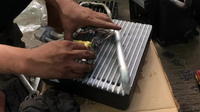 technician is assembling the heat exchanger evaporator component of a car on the street pavement. close up