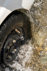 A car tire is in the water, and the water is splashing around it. The tire is black and has a bolt on it