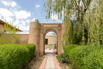 A brick archway leads to a courtyard with a brick wall and a stone wall. The courtyard is...
