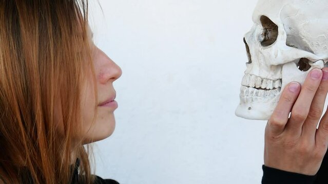 Close-up of a beautiful lady kissing a human skull on the teeth and cheek