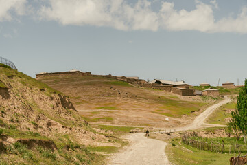 A dirt road winds through a dry, barren landscape. The sky is clear and blue, and there are no clouds in sight. The road is narrow and winding, and there are no other people or vehicles in the scene